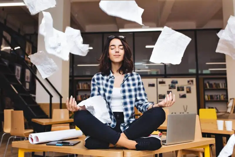 Woman at work meditating with papers flying around her