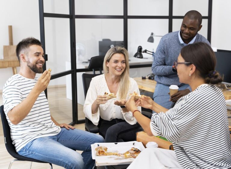 Employees sitting around a coffee table having pizza. One of the many HR Incentive Trends