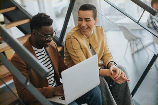 Two work friend collaborating while sitting on stairs in the office