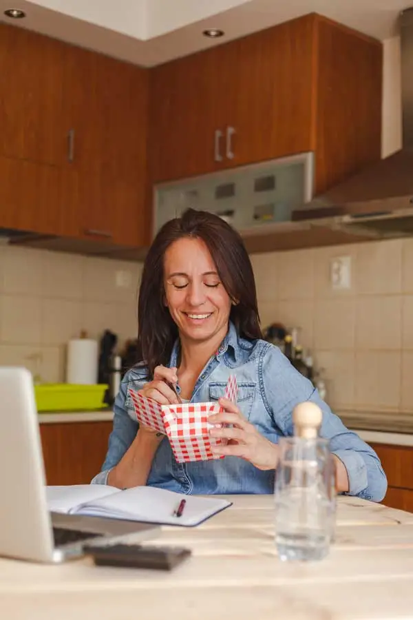 woman using laptop while eating food at home