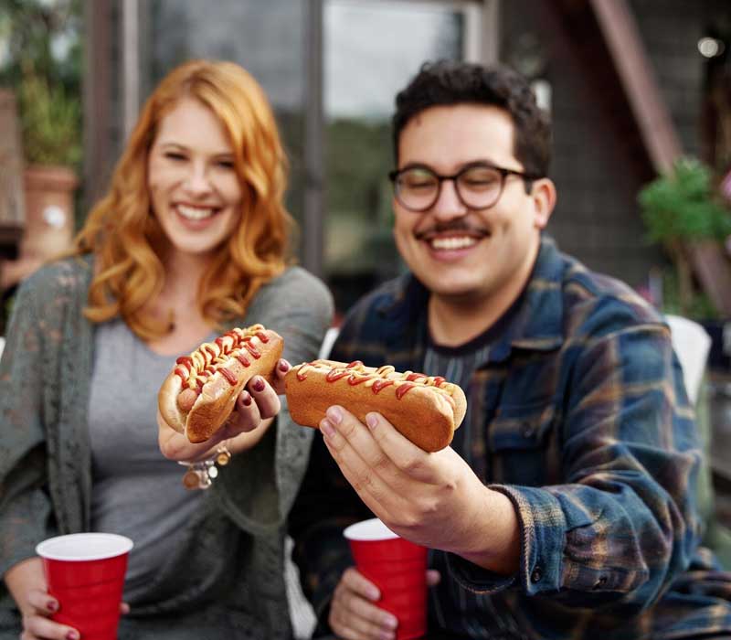 two colleagues holding hot dogs for national hot dog day celebration